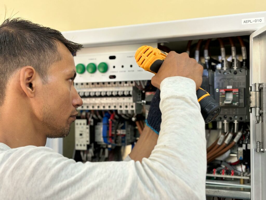 Professional electrician using a drill on an indoor circuit breaker panel.